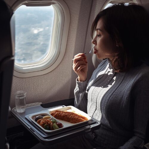 Traveller eating meal on plane with supplements beside tray